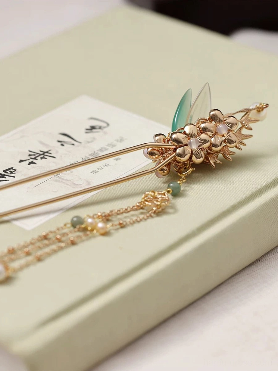 Side view of a traditional Chinese hair stick with pine-branch style metal decoration, floral ornament, and long beaded tassel resting on a vintage calligraphy book