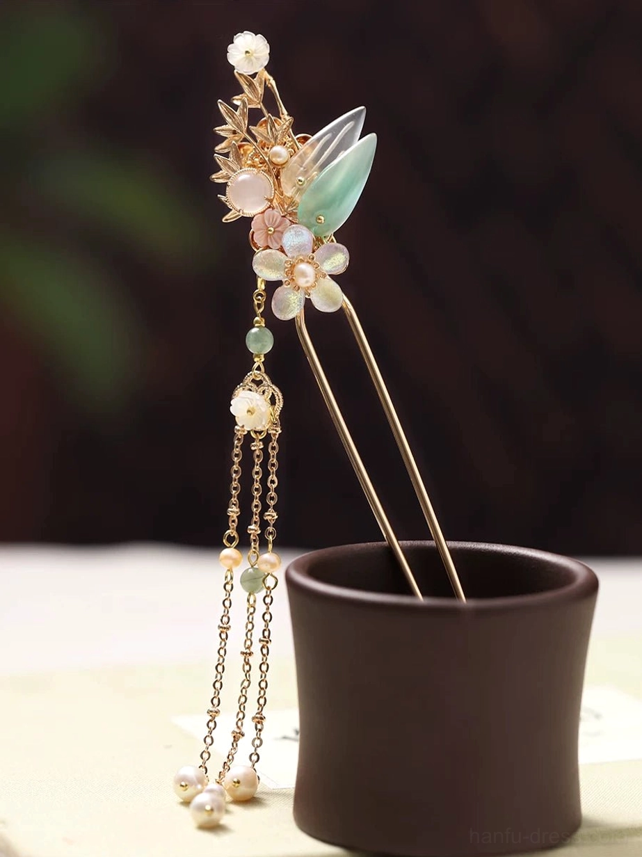 Traditional Chinese double-strand tassel hair stick with pink white flowers, jade-green leaves, gold-tone details, and pearl beads displayed in a dark ceramic cup