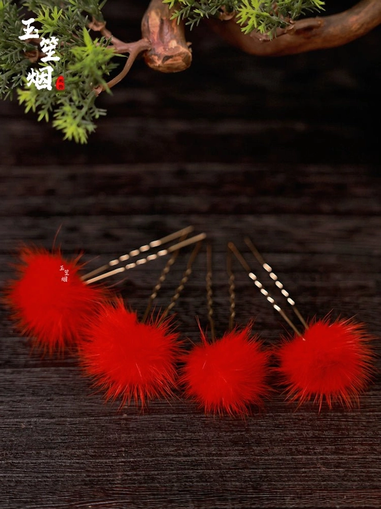 Four-piece red furball Hanfu hair pin set with golden U-shaped sticks arranged on dark wood with green plant accents