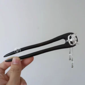 Hand holding a double-pronged fox Hanfu hair stick showing the smooth dark wood prongs and silver-tone dangling tassel