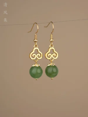 Front view of a pair of Chinese Ruyi jade earrings with polished gold hollow decorative frames and smooth dark green pendant beads suspended against a warm neutral background