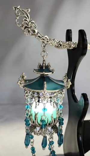 Front view of luminous Chinese lantern Hanfu hair stick displayed on a black wooden stand with teal layered roof silver filigree and blue bead tassels