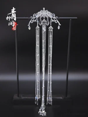 Traditional Chinese silver-tone back hair pin with floral filigree, clear waterdrop crystal pendants, and long layered tassels displayed on a black stand