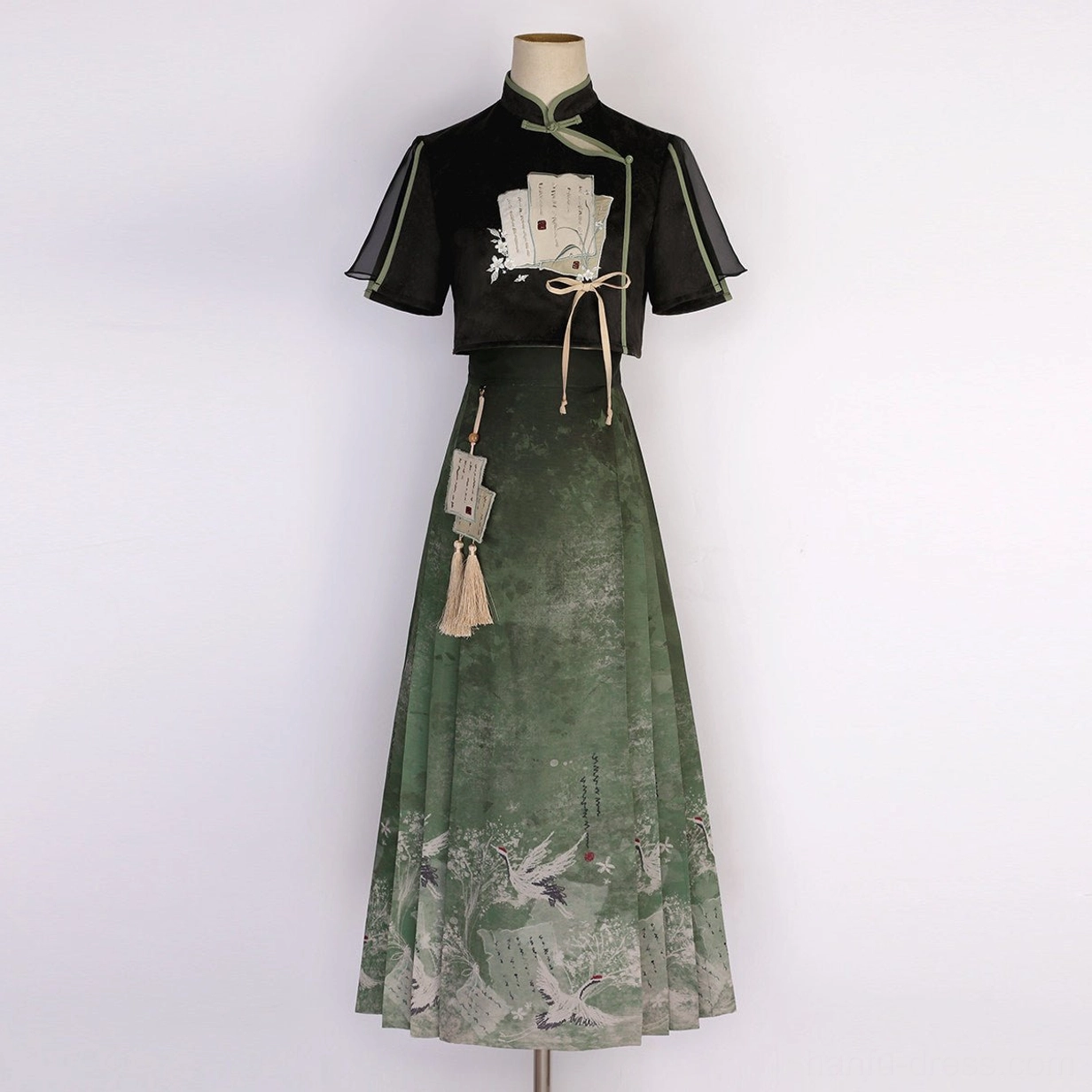 Full modern Hanfu two-piece set displayed on a mannequin showing the black crop top green printed mamianqun and tassel details