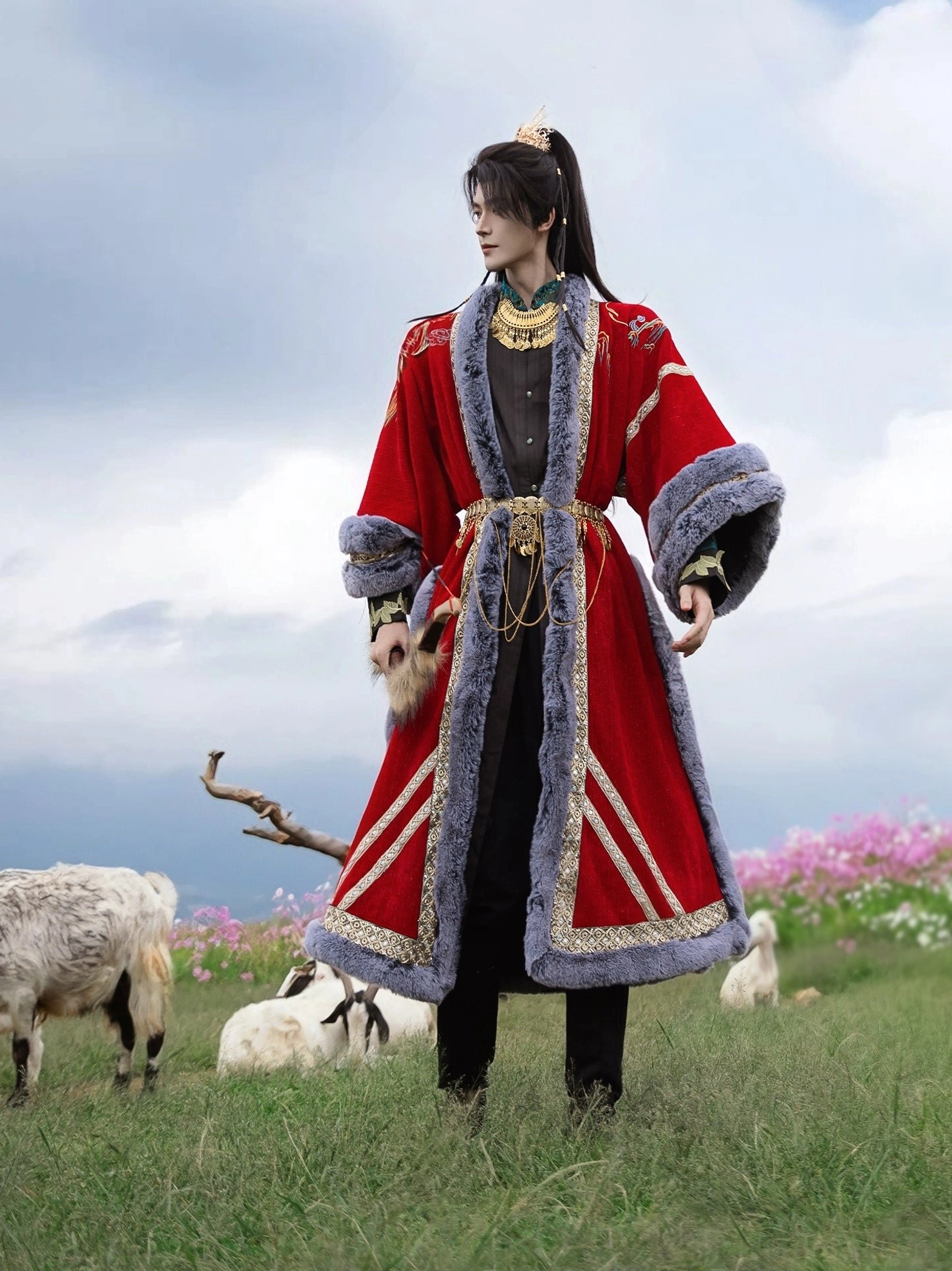 Full-body side view of a male model wearing a long red swordsman hanfu coat with gold hem stripes, fur cuffs, waist belt, and tassel details