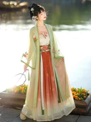 Side view of Gardenia themed Song Dynasty Hanfu set showing a translucent green floral embroidered outer coat, flowing gradient skirt, traditional hairstyle, and tassel fan in warm sunset garden light