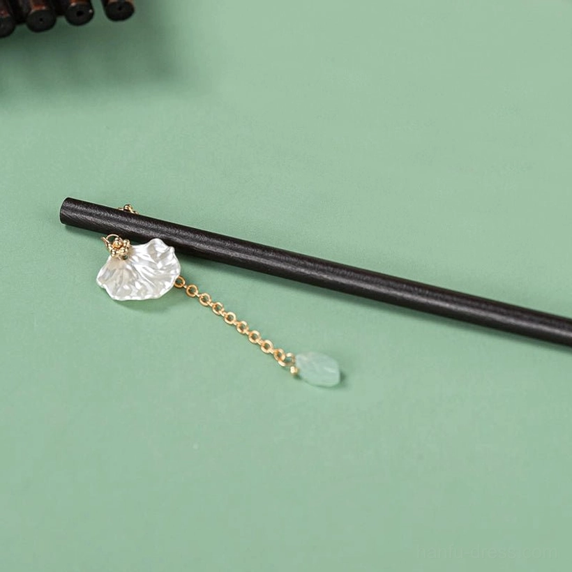 Dark wood Chinese hairpin stick with gold-tone tassel shell-style flower and pale green charm on green background