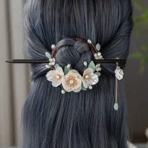 Gardenia wood Chinese hairpin worn at the back of a coiled updo with floral ornaments pearl accents green leaves and dangling tassel