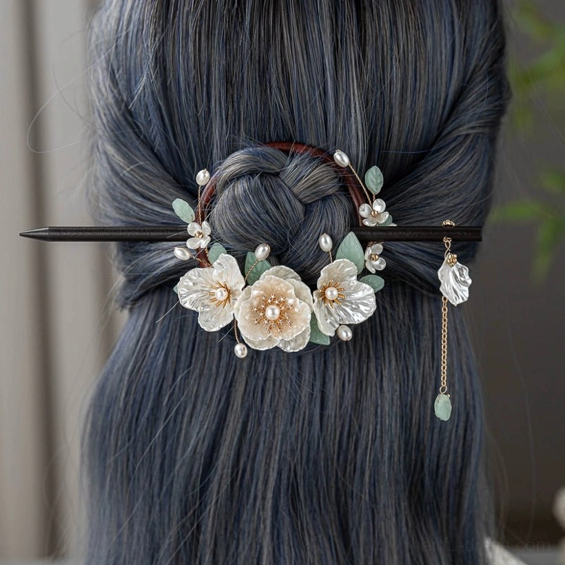 Gardenia wood Chinese hairpin worn at the back of a coiled updo with floral ornaments pearl accents green leaves and dangling tassel