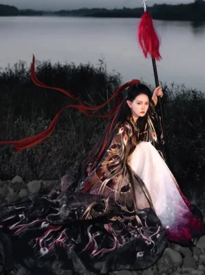 Three-quarter view of a General Mulan style Wei Jin Hanfu costume with feather embroidery, flowing red ribbon, wide sleeves, long gradient skirt, and decorative spear by the riverside