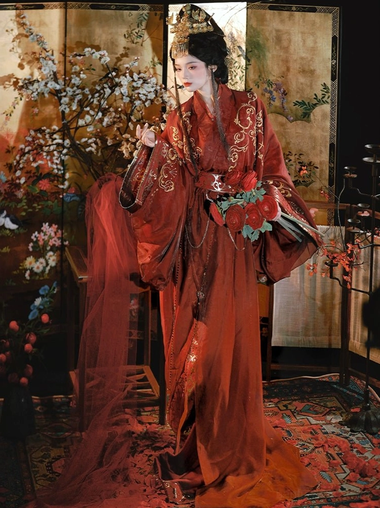 Three-quarter view of a woman holding a red silk flower bouquet while wearing a deep reddish-brown Han Dynasty Hanfu robe with gold embroidery, wide flowing sleeves, layered sash, and ceremonial styling