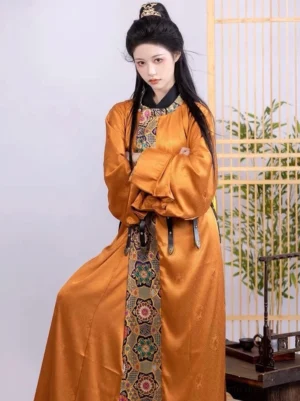 Front view of ginger Tang style Hanfu robe with round collar, golden satin-look fabric, Dunhuang-inspired floral brocade panels, and black waist belt