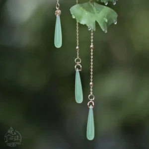 Close-up of golden tassel chains and jade-tone teardrop pendants on a green ginkgo leaf Chinese hair stick