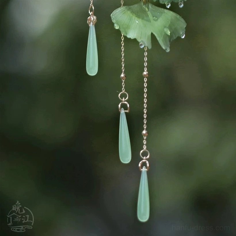 Close-up of golden tassel chains and jade-tone teardrop pendants on a green ginkgo leaf Chinese hair stick