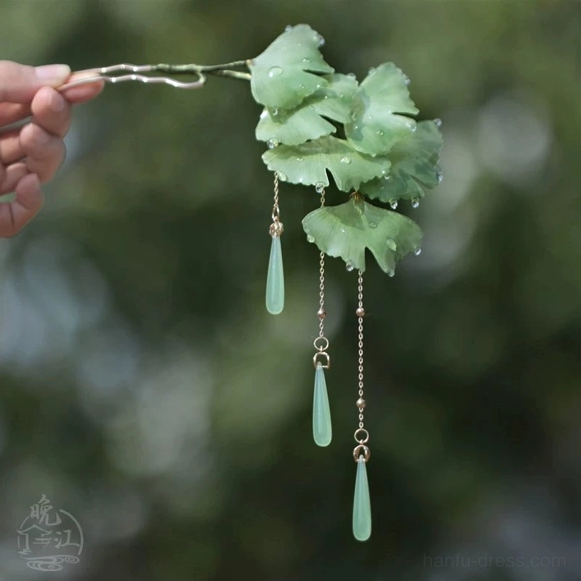 Green ginkgo leaf Chinese hair stick held in hand with dew-drop details, golden tassel chains, and jade-tone teardrop pendants
