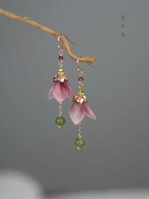 Glazed flower bud Chinese earrings hanging on a natural branch with mauve purple petals, gold calyx details, and green bead drops