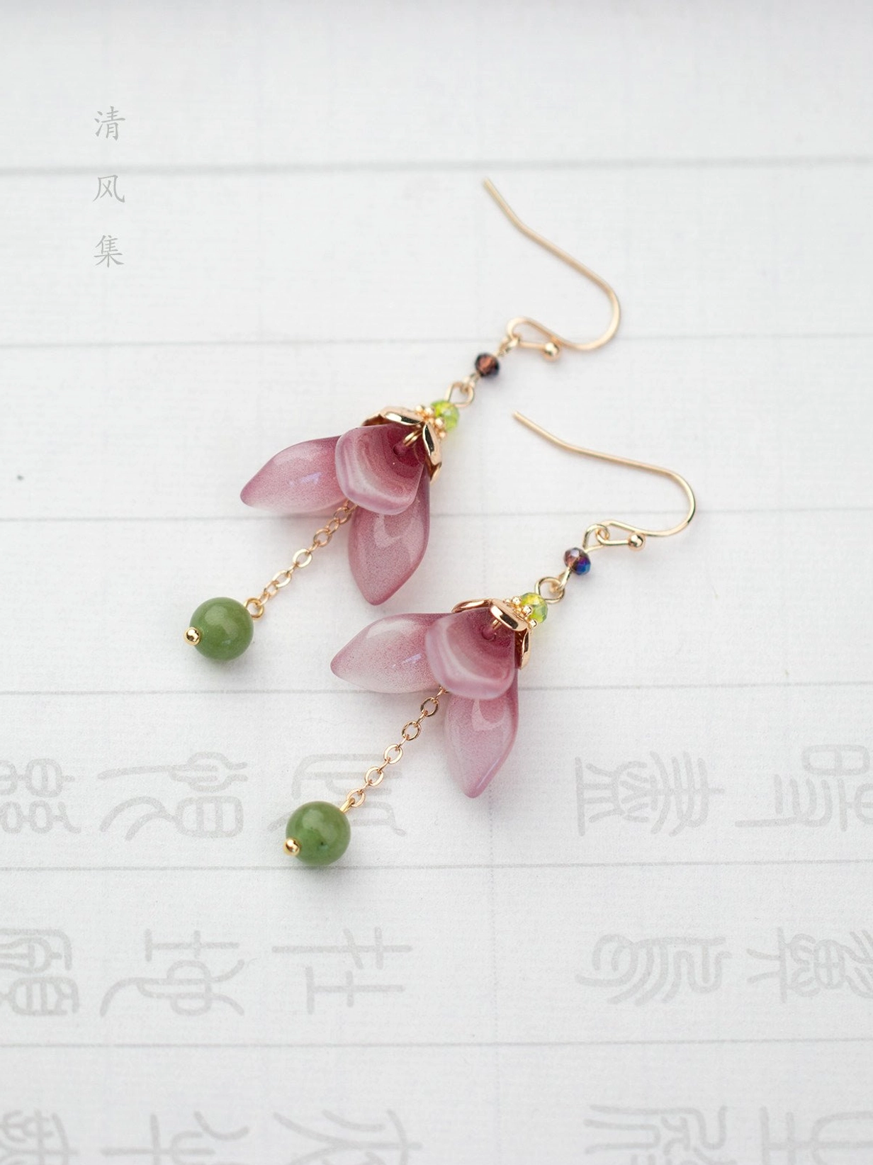Glazed flower bud Chinese earrings displayed on traditional rice paper with seal calligraphy, featuring purple petals and jade-like green beads
