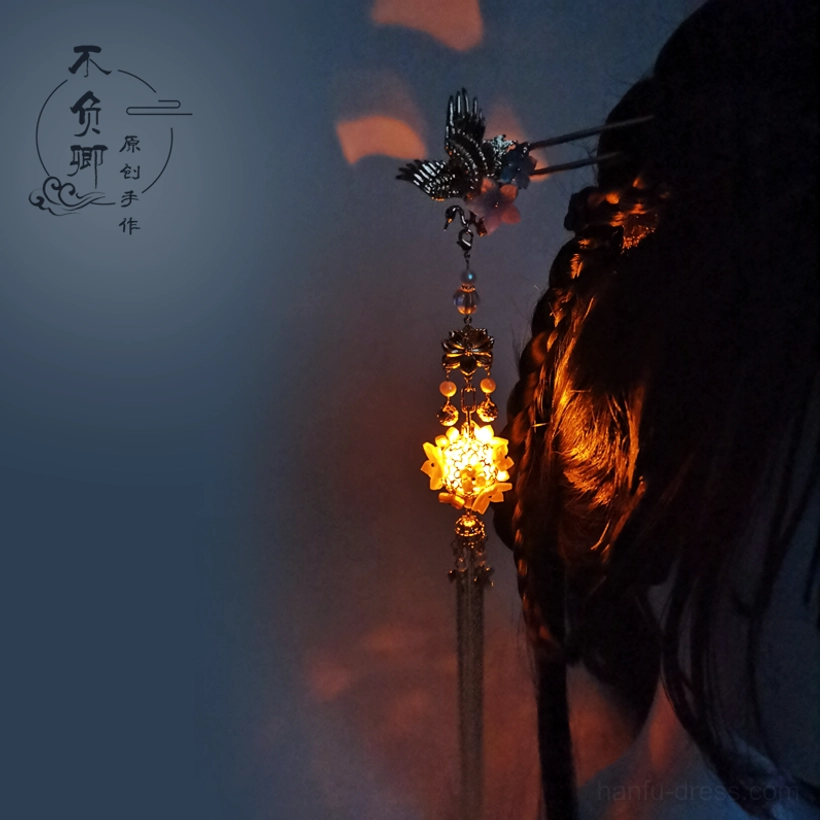 Glowing lantern Chinese hair stick with dark metal crane ornament, purple floral beads, golden lantern pendant, and long tassel worn in a braided Hanfu hairstyle