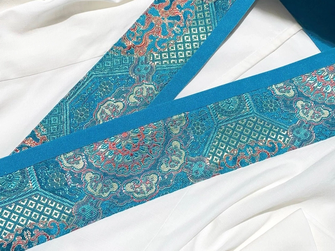 Close up of teal blue Chinese brocade trim with geometric floral pattern on God of War xianxia hanfu costume