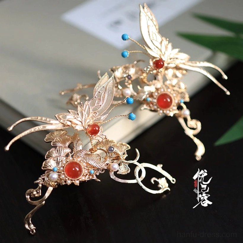 Gold crescent butterfly traditional Chinese hair pin with red agate, blue glazed beads, and small pearls on a dark tabletop