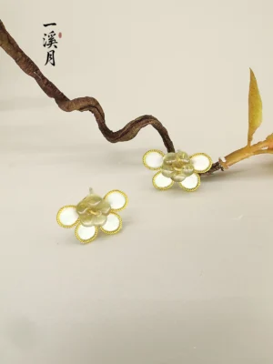 Plum blossom flower stud earrings with visible posts arranged with a natural branch on a light gray background