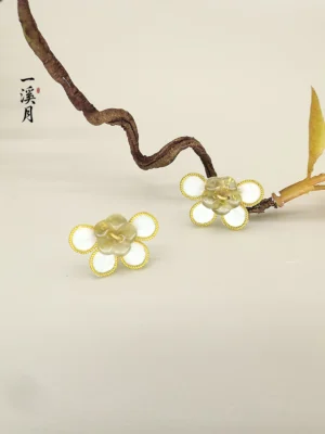 Gold-edged plum blossom stud earrings with two-tone petals displayed beside a twisted branch, Chinese floral jewelry