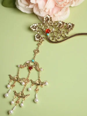 Ornate gold filigree hanfu hairpin with red and turquoise bead accents and dangling pearl tassels displayed with pink peony flowers