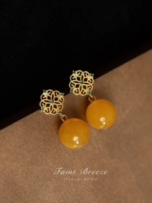 Close-up of elegant Chinese earrings featuring intricate gold flower filigree, glossy round amber-colored beads, and a refined vintage East Asian jewelry design