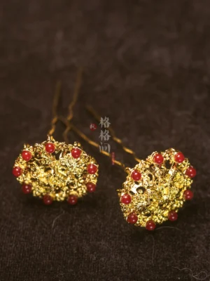 Pair of gold lotus filigree hair pins with round red glass bead accents and double prongs displayed on dark brown velvet fabric