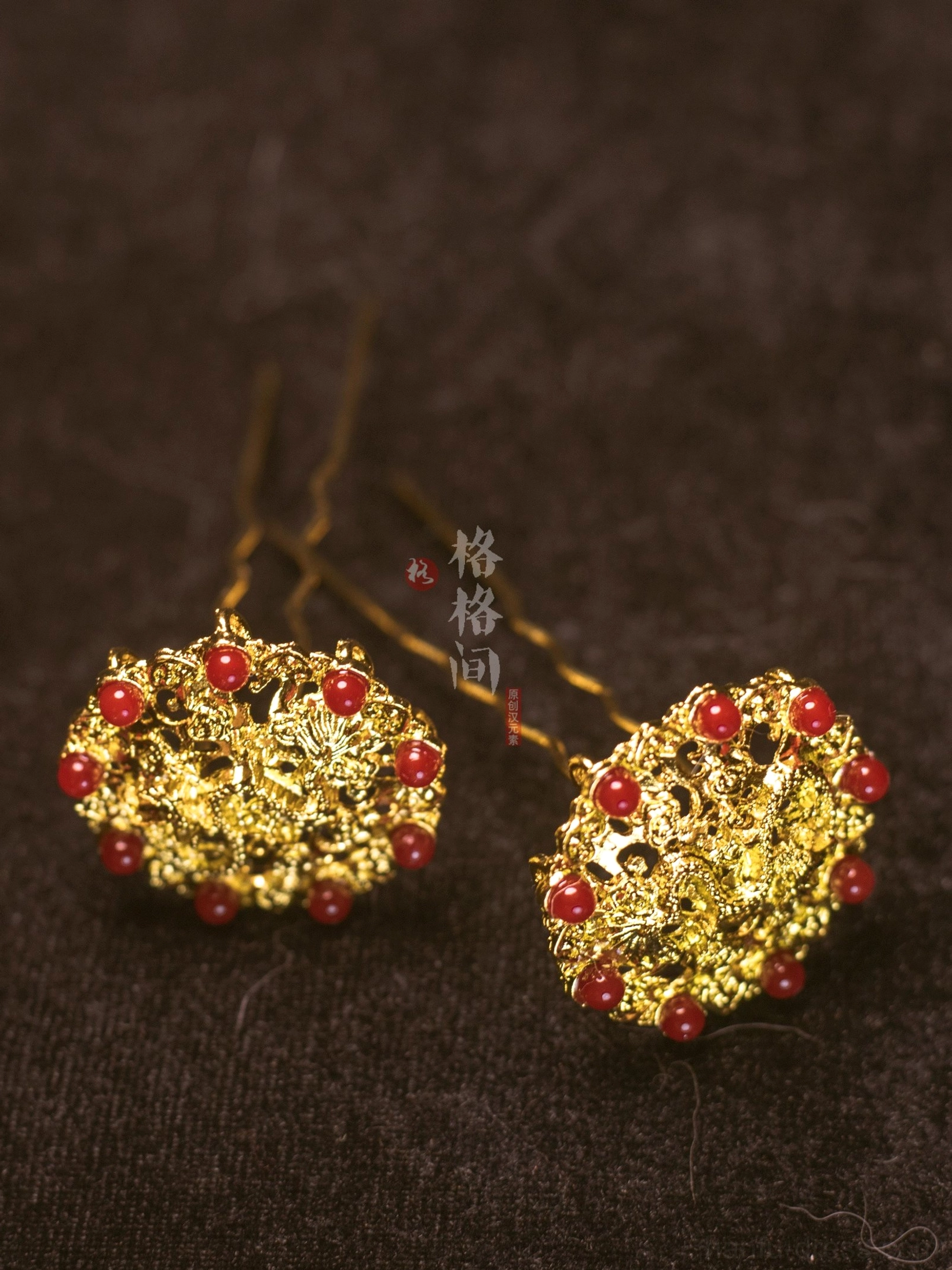 Pair of gold lotus filigree hair pins with round red glass bead accents and double prongs displayed on dark brown velvet fabric