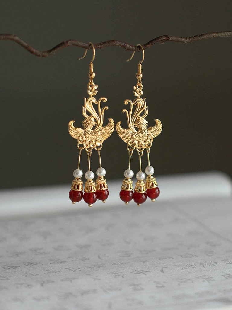 Gold phoenix Hanfu earrings with polished metal filigree pearl and red agate style bead tassels photographed beside handwritten Chinese calligraphy