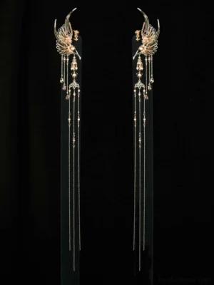 Pair of gold-tone phoenix tassel ear cuffs displayed on black background with ornate filigree birds, long chain tassels, and bead pendants