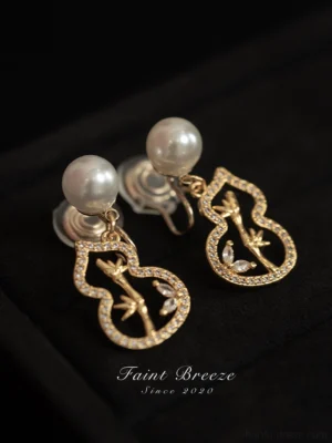 Golden bamboo gourd Chinese Hanfu stud earrings with zircon-paved outline and engraved bamboo motif on black fabric background