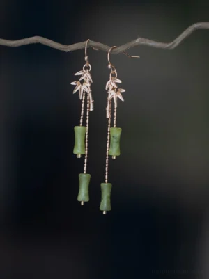 Golden bamboo leaf Hanfu earrings hanging from a natural twig, featuring rose gold toned bamboo charms, green bamboo joint beads, and delicate long drop chains