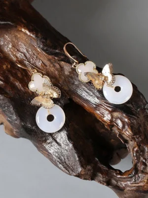 Golden butterfly and milky white jade-style peace buckle Chinese clip-on earrings displayed on a vintage wooden surface
