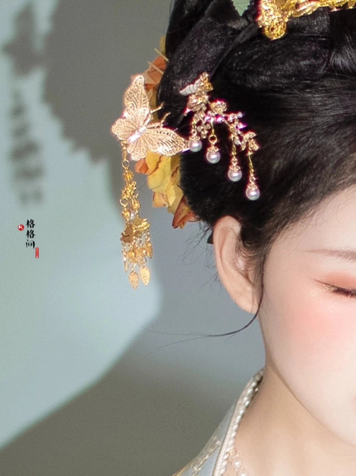 Close-up side view of a golden butterfly tassel hair pin with pearl-like pendants styled in a traditional Chinese hairstyle with a floral hair ornament