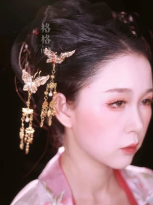 Woman wearing golden butterfly tassel hair pins with a traditional Chinese updo and pink Hanfu dress, showing elegant movement in the dangling ornaments