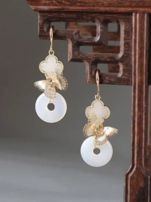 Front view of Chinese butterfly drop earrings with four-petal floral tops and white peace buckle pendants on carved wood