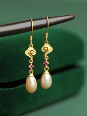 Golden cloud pearl drop Hanfu earrings with matte gold auspicious cloud charms, rose-red accents, teardrop pearls, and 925 silver hook ear wires displayed on green velvet