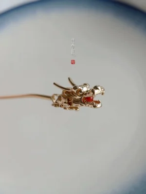 Top view of golden Chinese dragon hairpin with red gemstone detail displayed on blue and white ceramic plate