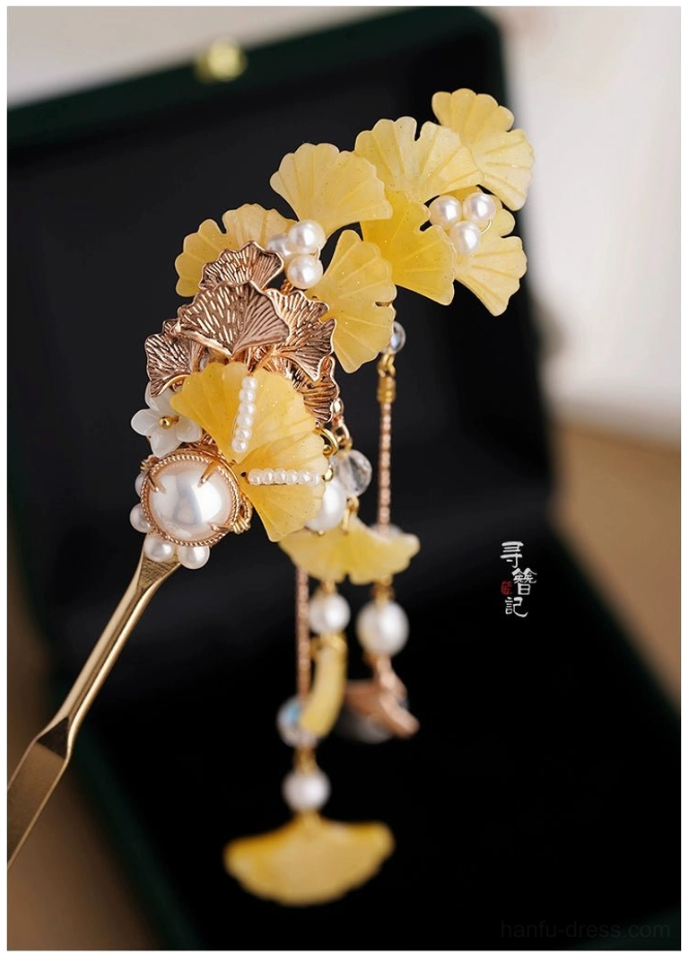 Close up of a golden ginkgo Hanfu hairpin featuring rose gold tone details, resin leaves, pearl embellishments, and flowing tassel pendants