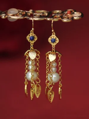 Golden gourd pearl tassel Chinese earrings for Hanfu displayed on a vintage jewelry bar against deep red fabric, with blue beads and gold leaf pendants