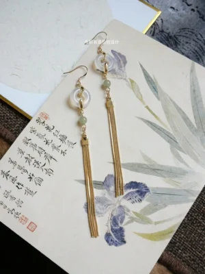 Oblique view of a pair of golden jade tassel Hanfu earrings displayed on traditional Chinese floral calligraphy art paper