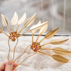 Close-up of two golden leaf hair pins with red floral gemstone centers and polished U-shaped bases for Hanfu hairstyles