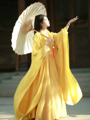 Side view of a golden yellow Wei Jin Dynasty hanfu robe made from lightweight sheer chiffon, featuring wide flowing sleeves, a red tassel detail, and a floor-length silhouette with a vintage oiled paper umbrella