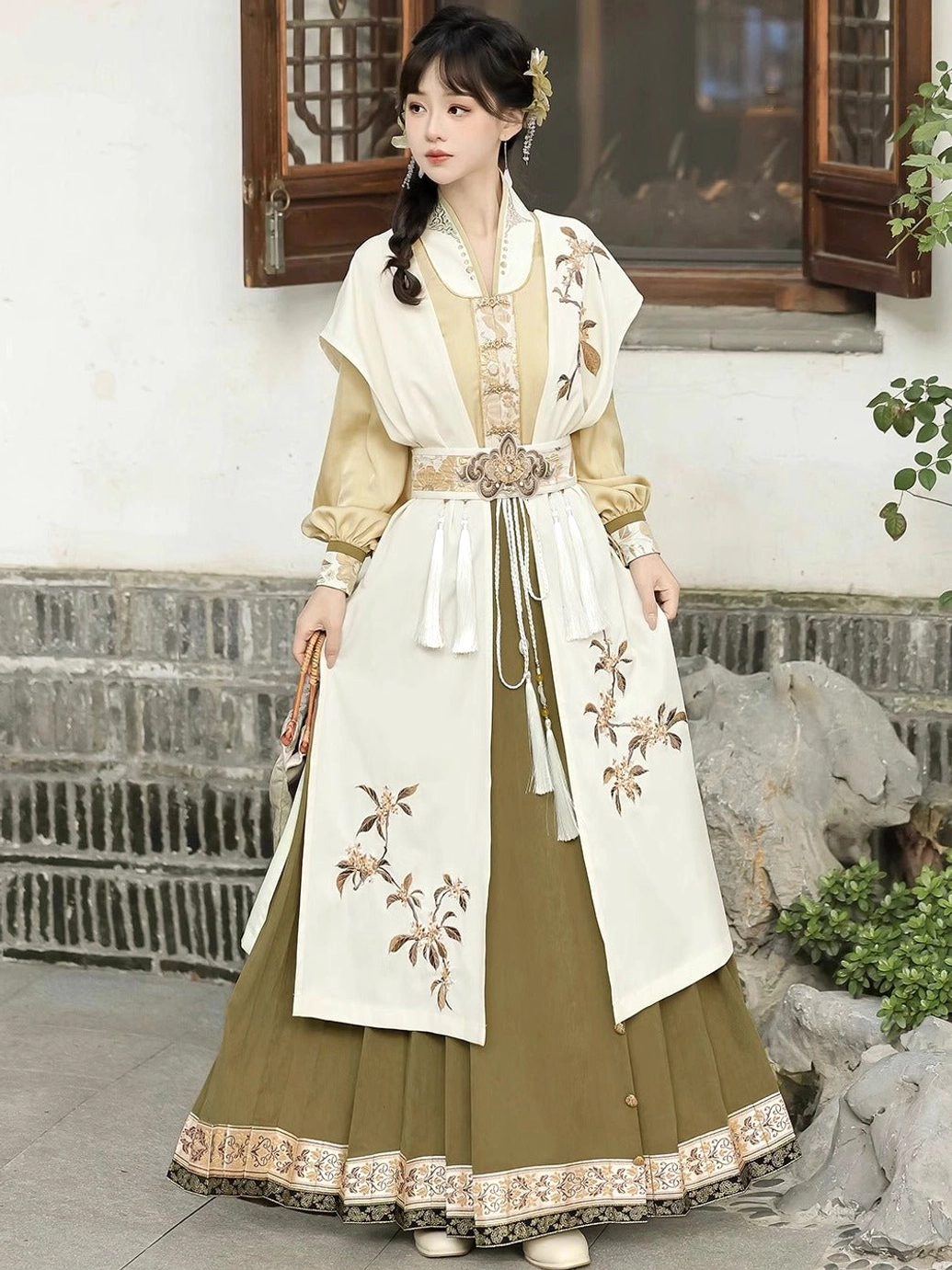 Side view of modern Ming Dynasty Hanfu set with golden yellow top, cream osmanthus embroidery and olive green horse face skirt holding a folding fan