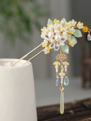 Golden osmanthus tassel Chinese hair stick with pearl-look beads green leaves and clear drop pendants displayed on a white ceramic cup