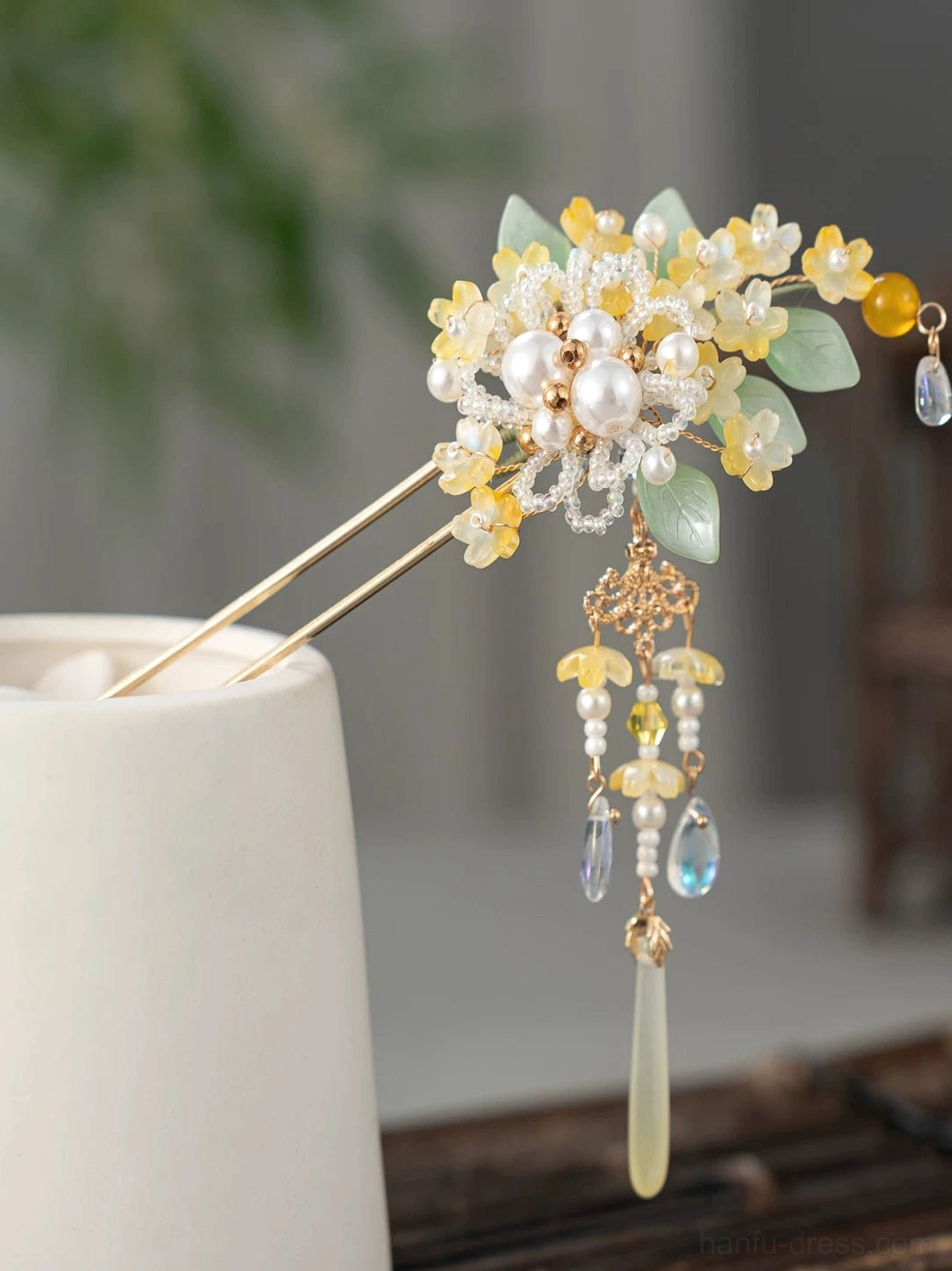 Golden osmanthus tassel Chinese hair stick with pearl-look beads green leaves and clear drop pendants displayed on a white ceramic cup
