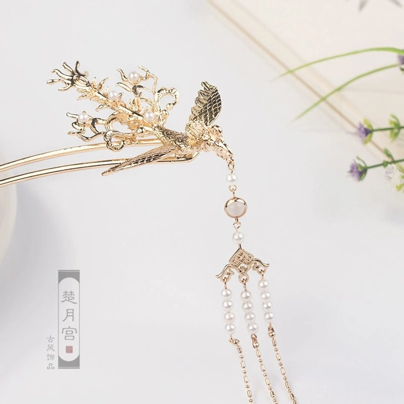 Close-up golden phoenix tassel hairpin featuring carved phoenix and floral crown details clustered pearl-style tassels and a gem bead