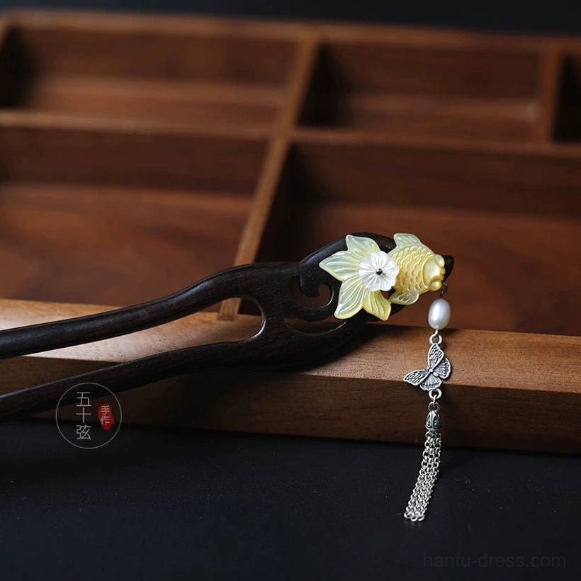 Close side view of Golden Scales Chinese hair stick with golden fish, white floral detail, dark wood-style base and long metal tassel